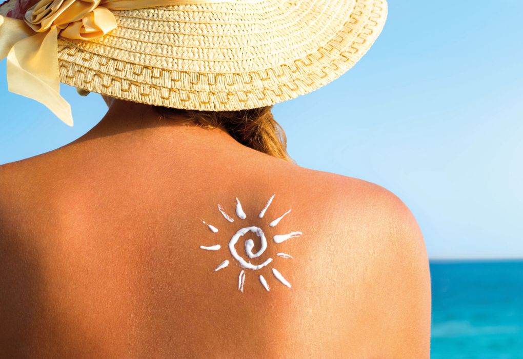 Eine Frau mit Sonnenhut von hinten fotografiert, auf ihrem Rücken ist eine Sonne aus Sonnenmilch zu sehen.