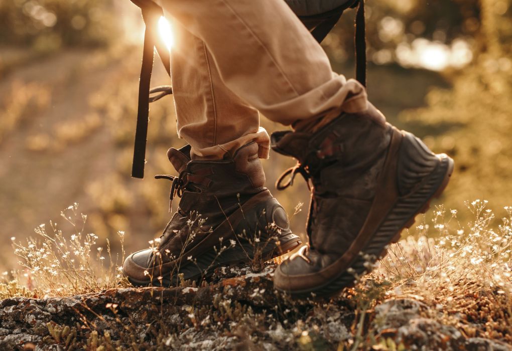 Person mit Wanderstiefeln läuft mit Trekkingstöcken über einen sonnigen Waldweg