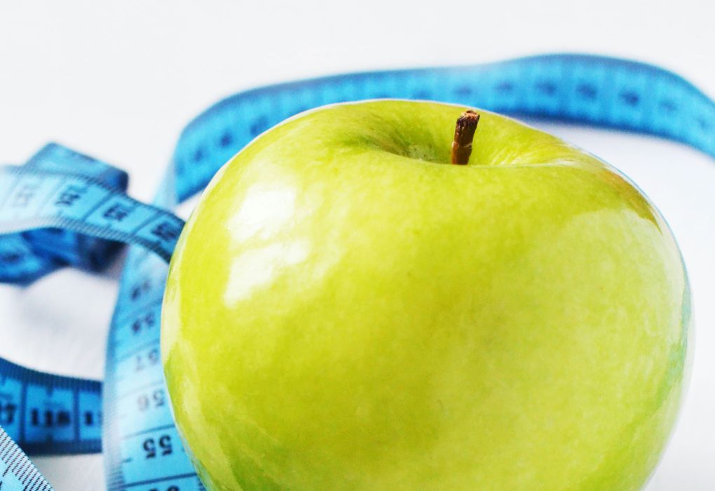 Grüner Apfel mit Maßband auf blauem Hintergrund