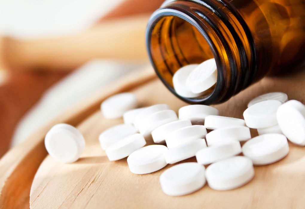 Braune Glasflasche mit weißen Tabletten, Schüßler-Salze auf hellem Holzuntergrund