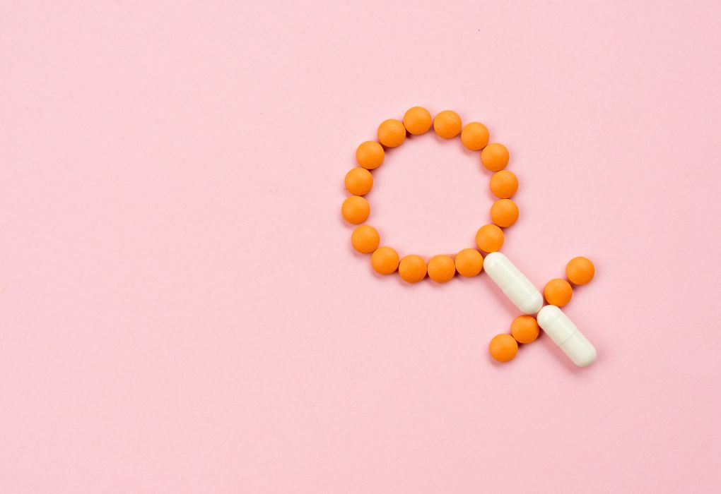 Molekülmodell in Form des weiblichen Hormon-Symbols aus orangen Kügelchen auf rosa Untergrund