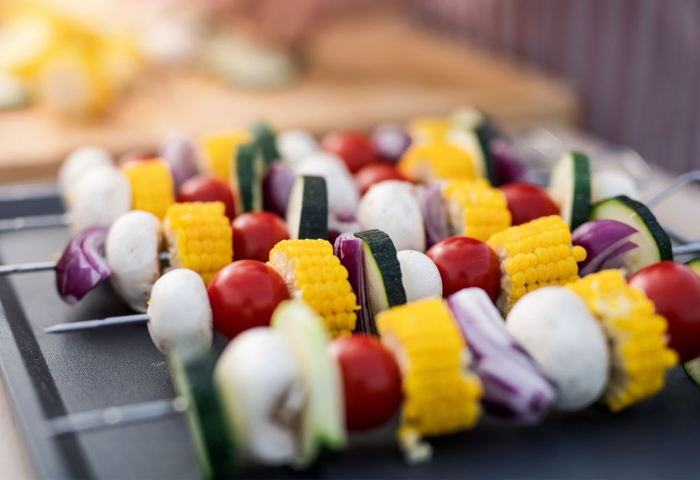 Bunte Gemüsespieße mit Paprika, Zucchini und Mais liegen auf einem Grillrost