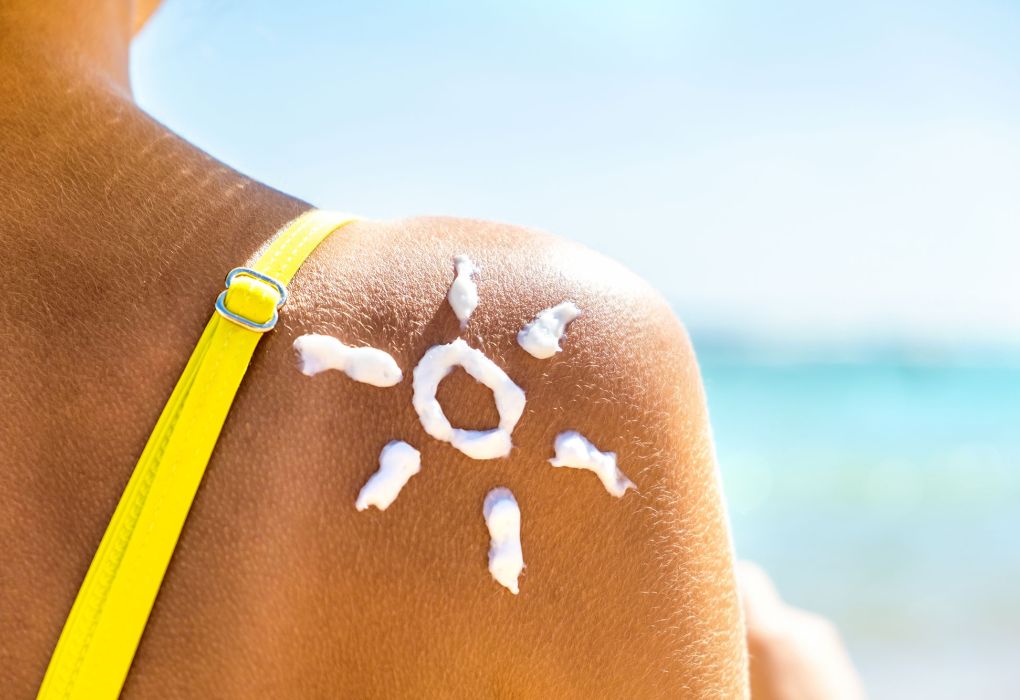 Frau mit Sonnencreme-Symbol in Form einer Sonne auf der Schulter am Strand