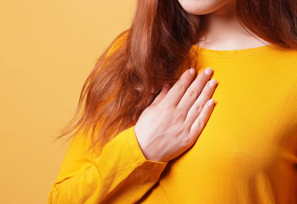Frau in gelbem Pullover hält sich die Brust