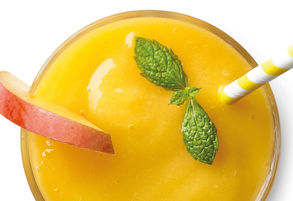 Glas mit orangem Smoothie, Strohhalm, garniert mit Apfel und Minze.