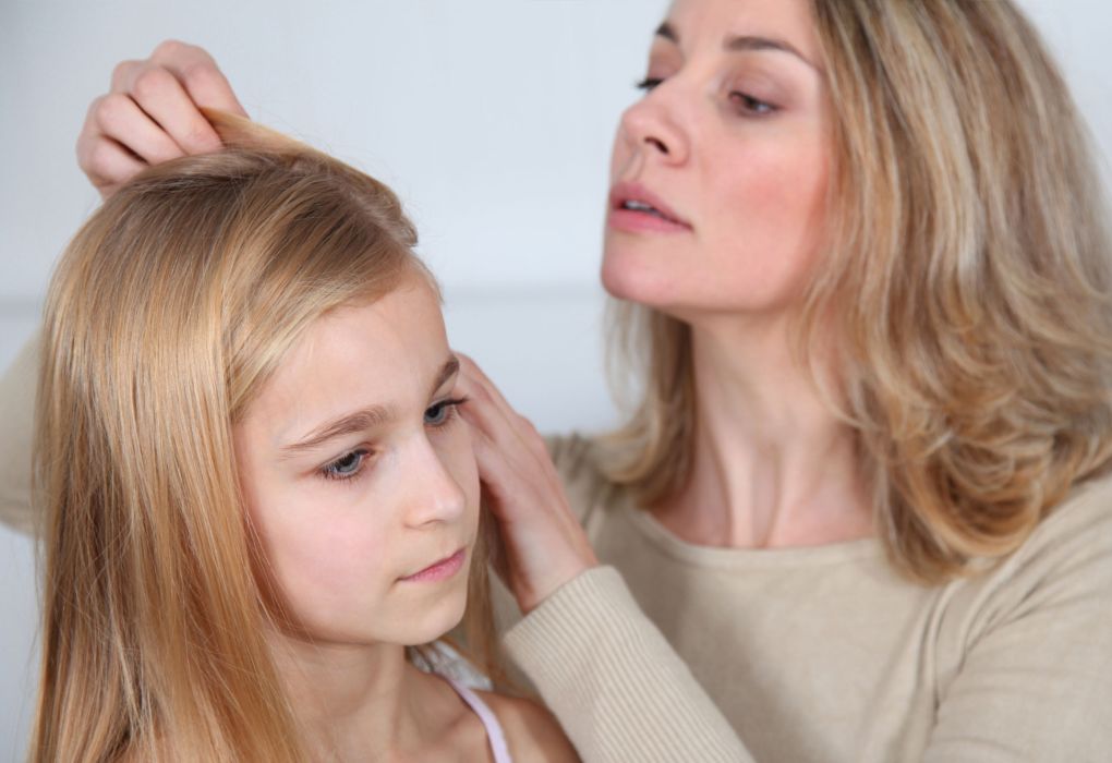 Frau kontrolliert das Haar eines Mädchens sorgfältig auf Kopfläuse