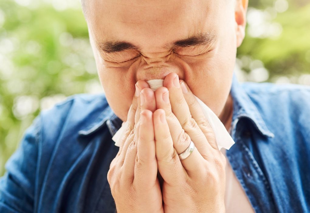 Mann niest in ein Taschentuch, Symbol für Pollenallergie und Heuschnupfen