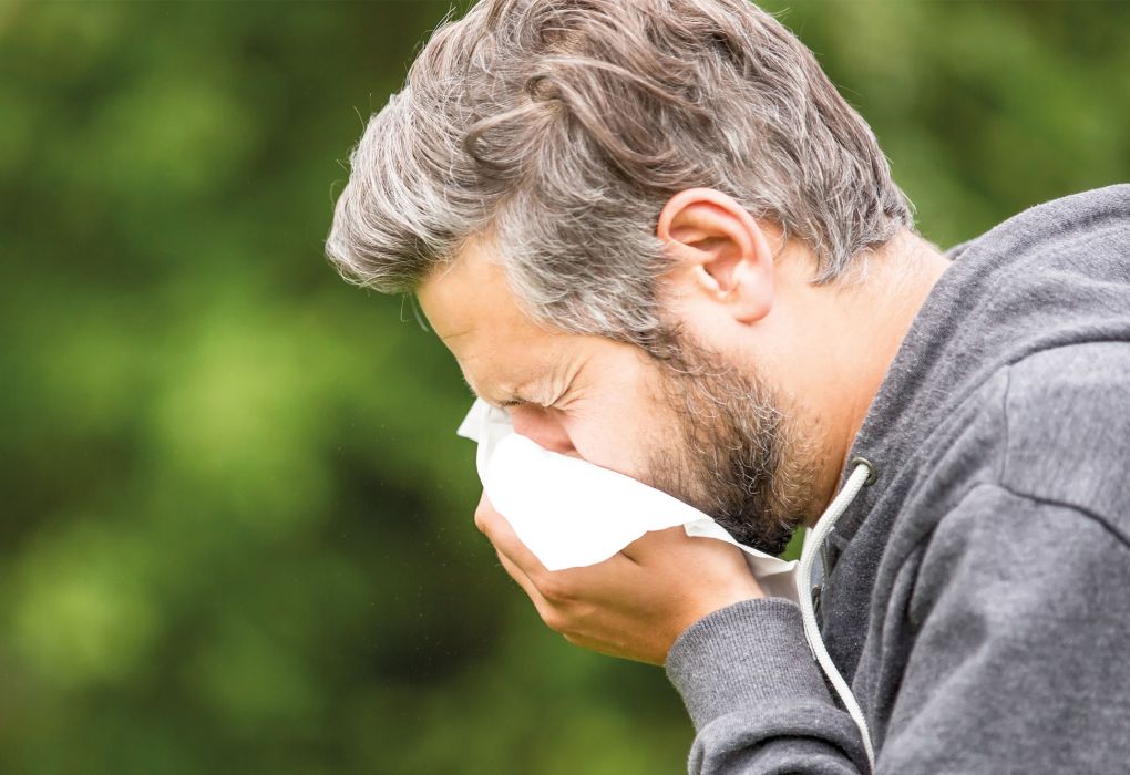 Mann niest in ein Taschentuch im Freien