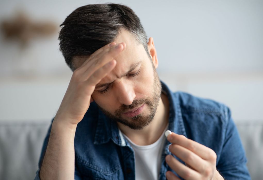 Mann fasst sich an die Schläfe und hält Schmerztablette in der Hand