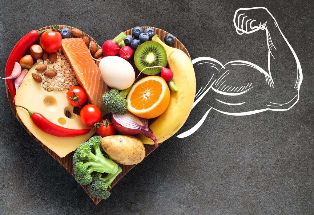 Herz aus Obst und Gemüse neben einer gezeichneten Muskelarm-Silhouette auf schwarzem Hintergrund