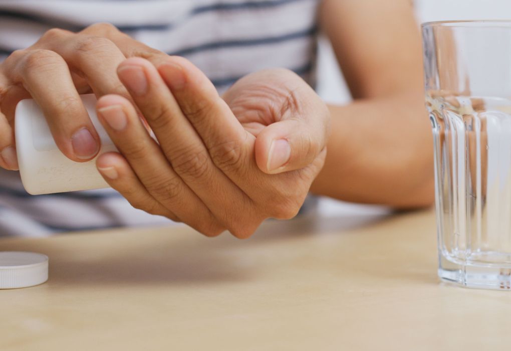 Mann legt eine Tablette in die Hand und hält daneben ein Glas Wasser