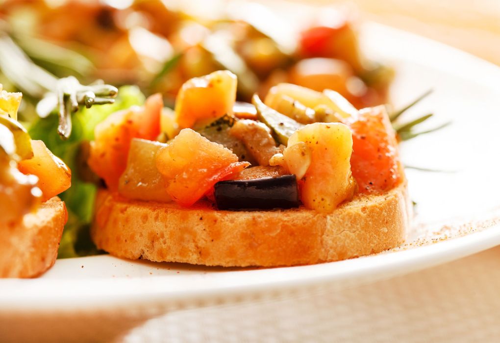 Teller mit gerösteten Baguettescheiben, belegt mit Tomaten, Kräutern und Olivenöl