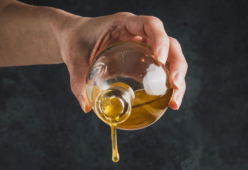 Eine Person schenkt Öl aus einer Glaskaraffe aus.