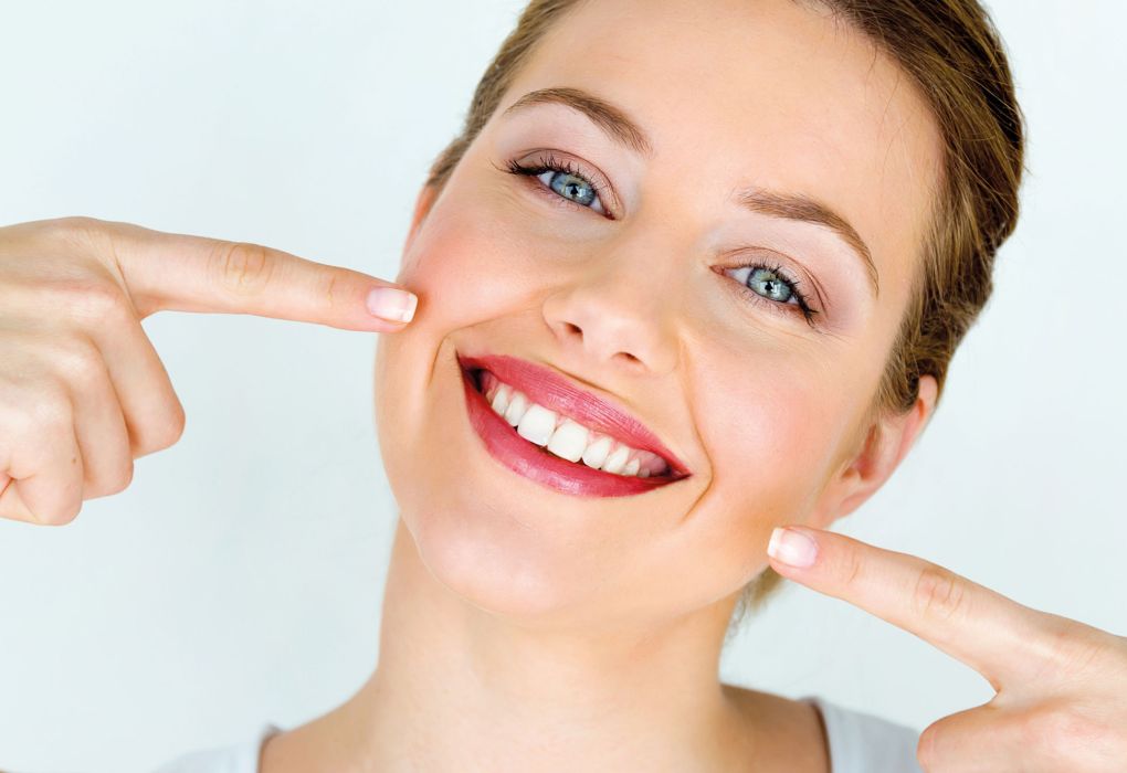 Junge Frau zeigt auf ihr strahlendes Lächeln mit weißen, gepflegten Zähnen