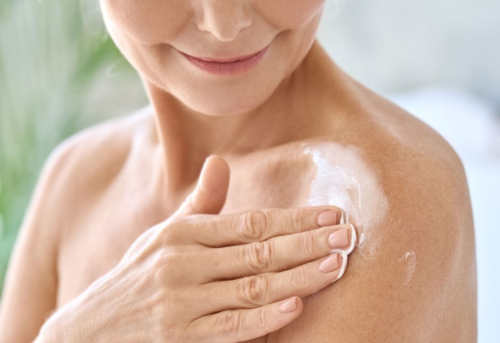 Frau trägt weiße Creme auf ihre Haut auf, um trockene oder gereizte Haut zu pflegen