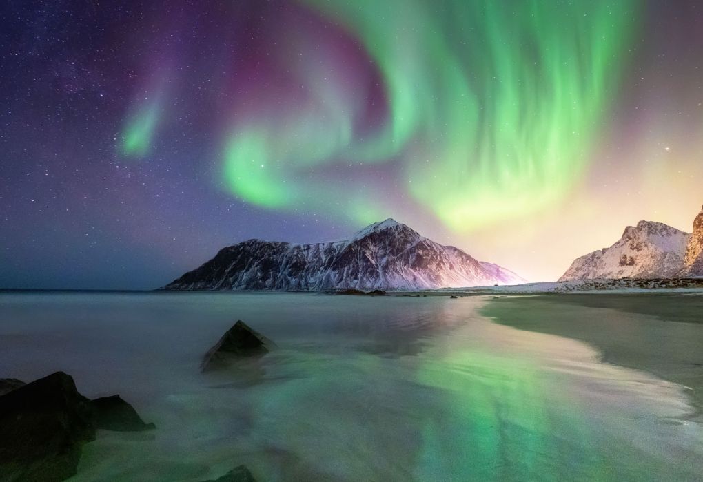 Farbintensive Polarlichter leuchten am Nachthimmel über verschneiten Bergen und Küste