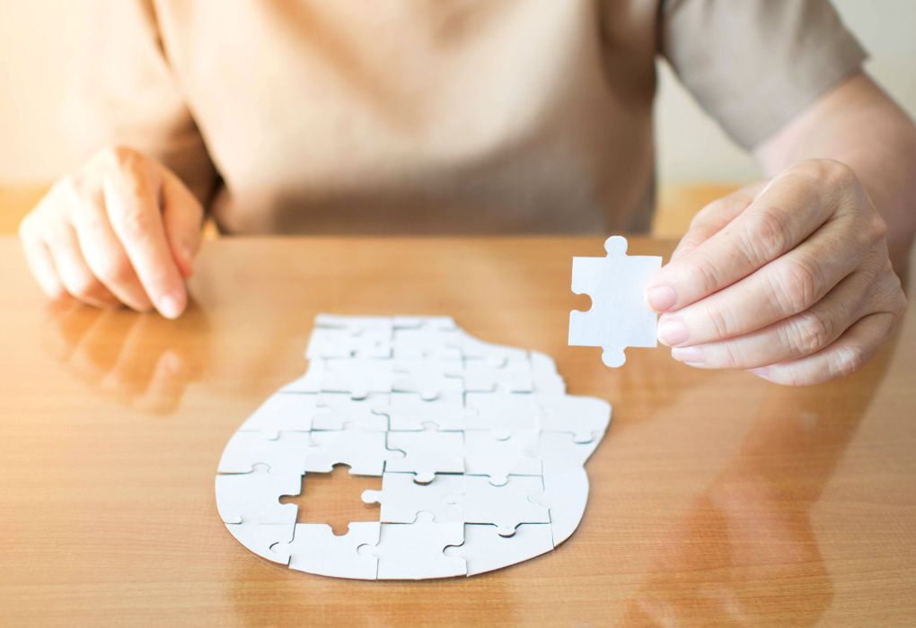 Person setzt ein weißes Puzzle in Form eines menschlichen Kopfes zusammen