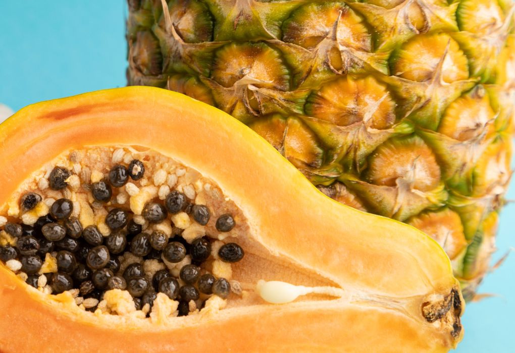 Aufgeschnittene Papaya mit Kernen und eine Ananas nebeneinander