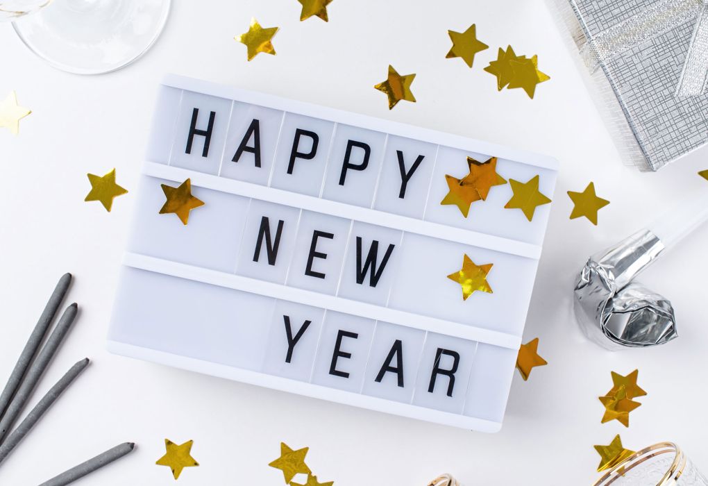 Leuchtbox mit Schriftzug „Happy New Year“ umgeben von goldenen Sternkonfetti und Partyaccessoires