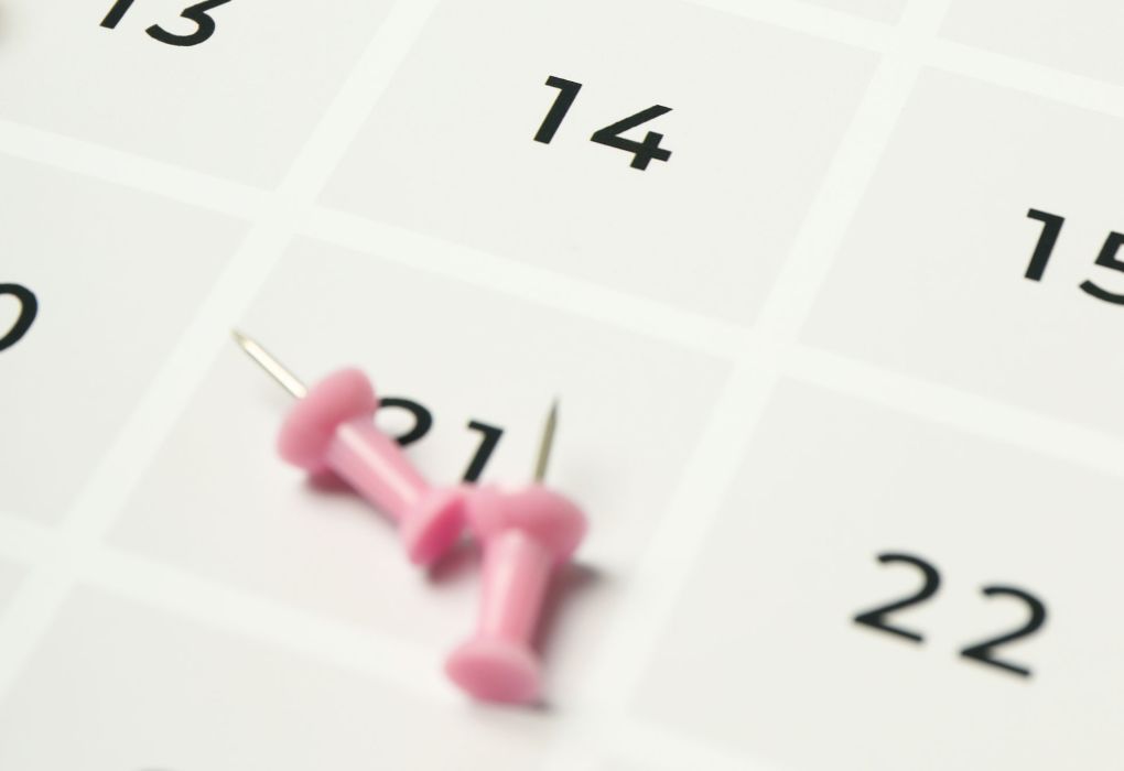 Nahaufnahme eines Kalenders mit eingestecktem rosa Pin bei einem Datum