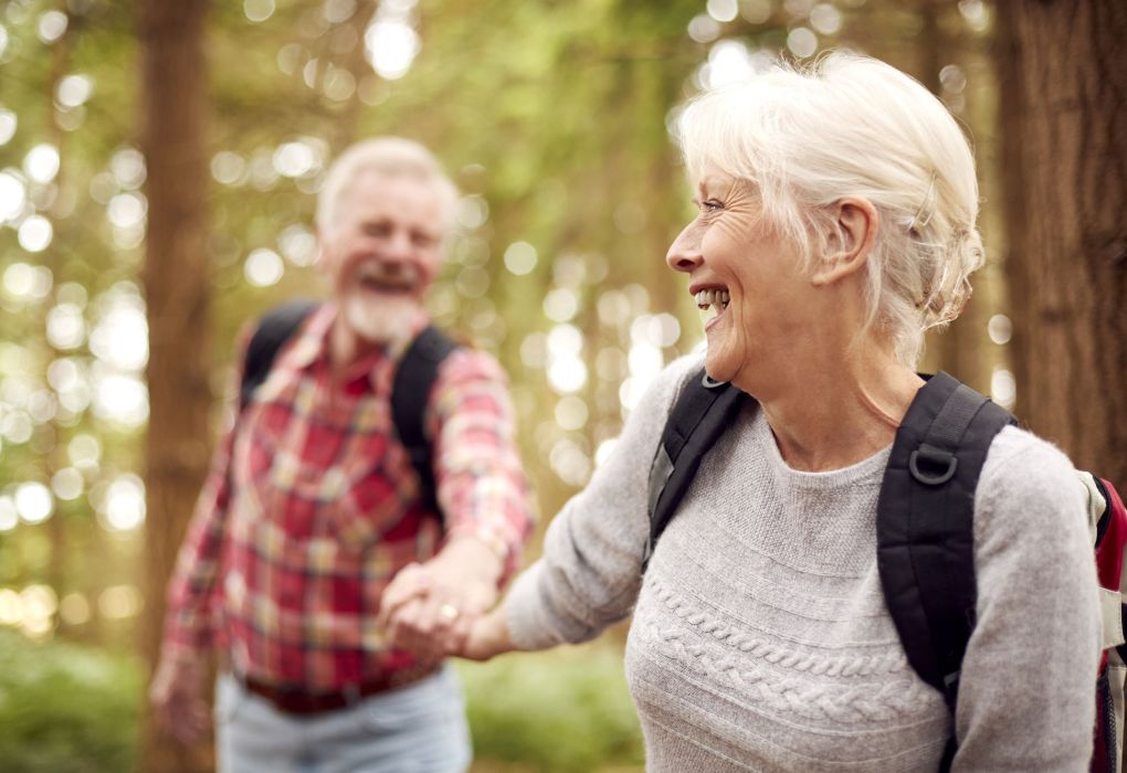 Zwei ältere Personen lachen im Wald und halten sich an den Händen.