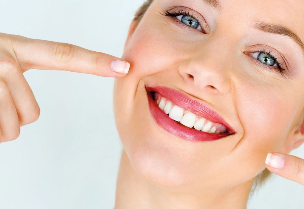 Eine lächelnde Frau zeigt auf ihre gesunden, weißen Zähne.