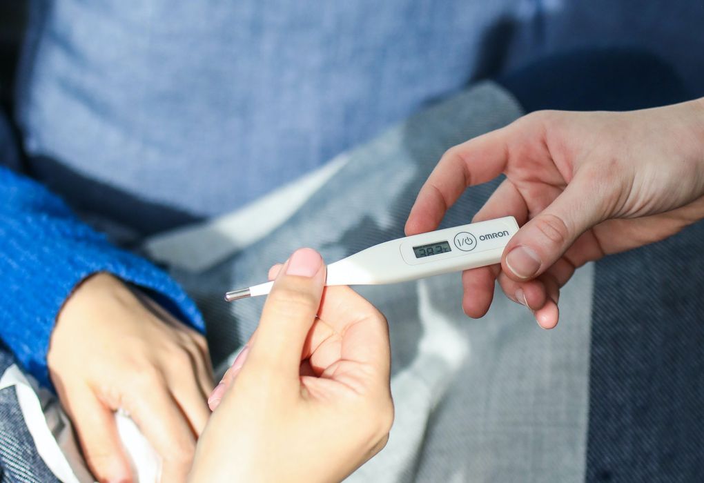 Hand hält ein digitales Thermometer, das Fieber anzeigt.