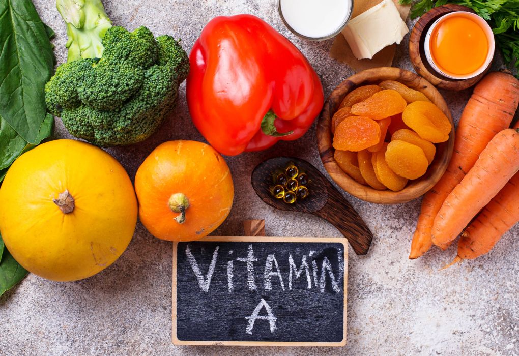 Verschiedene Lebensmittel wie Karotten, Paprika, Brokkoli und Aprikosen mit Tafel „Vitamin A“