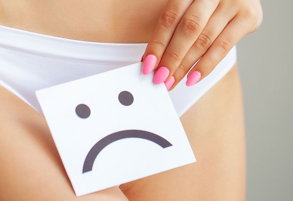 Frau hält ein Blatt Papier mit traurigem Smiley vor den Slip