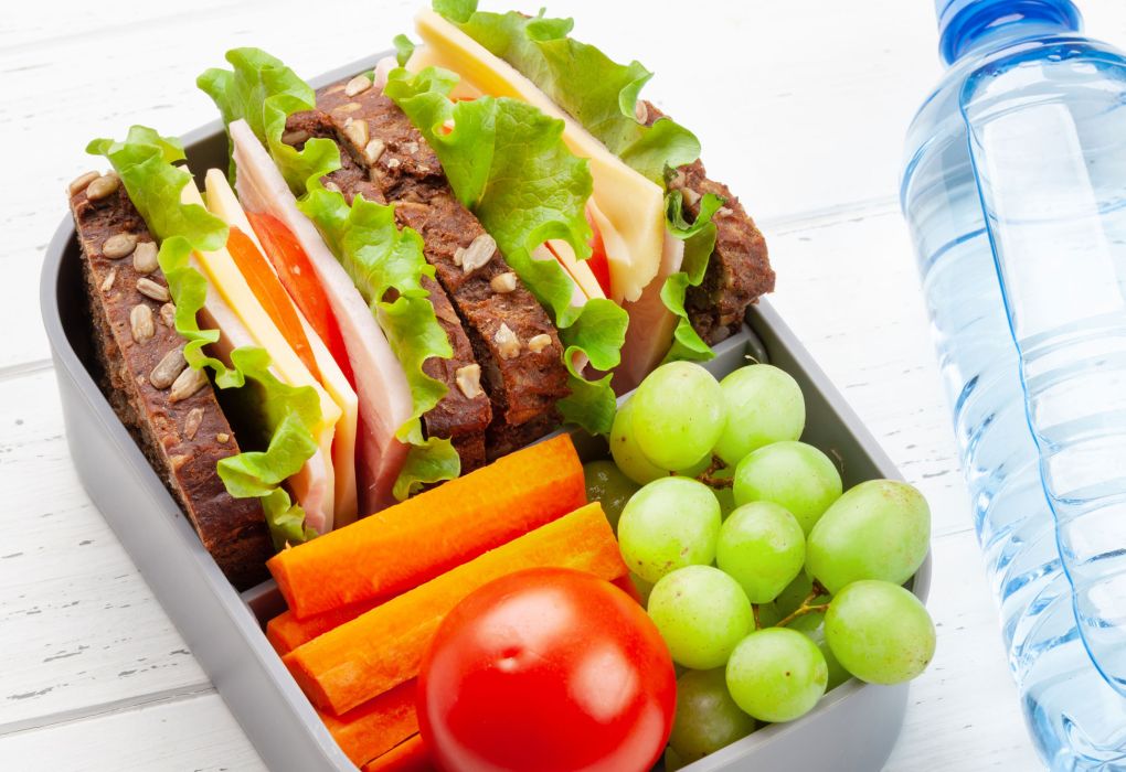 Brotdose gefüllt mit Sandwich, Tomaten, Weintrauben und Wasserflasche