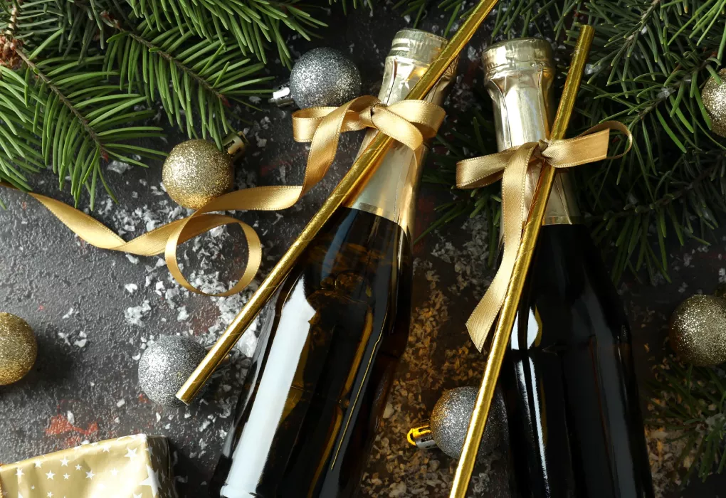 Dekorierte Champagnerflaschen mit goldenen Bändern zwischen Tannenzweigen und Weihnachtsdeko