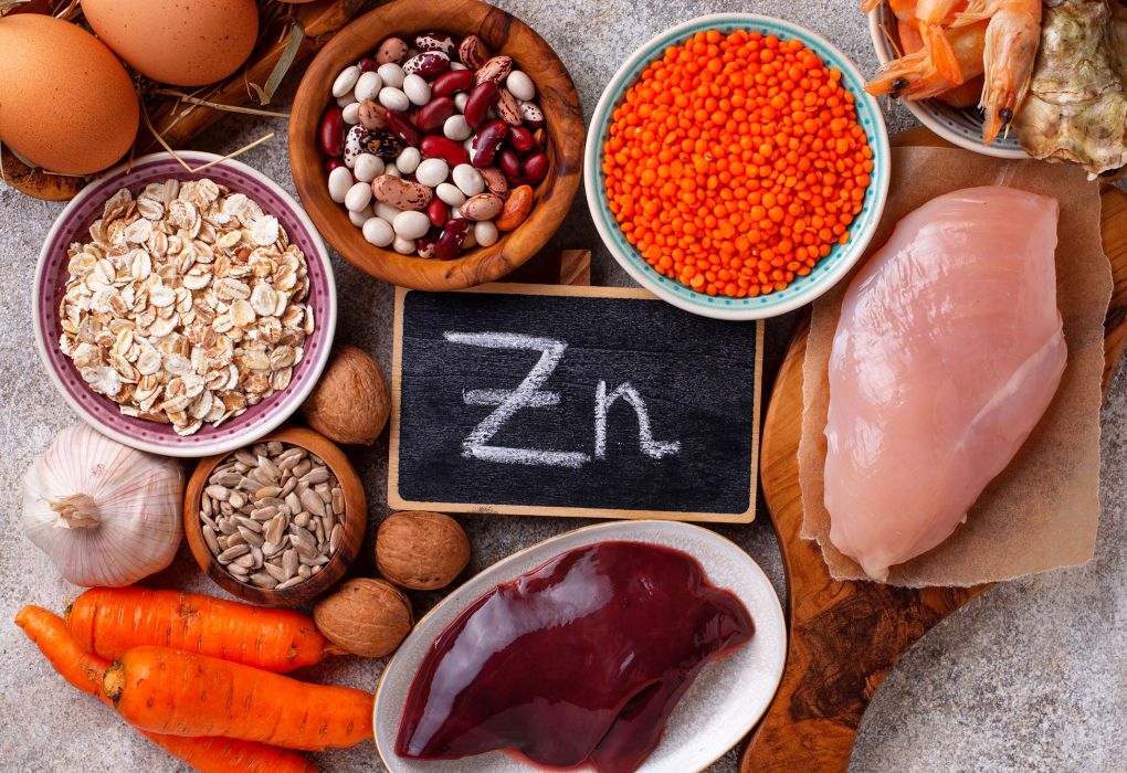 Verschiedene Lebensmittel wie Nüsse, Linsen, Fleisch und Eier umgeben eine Kreidetafel mit der Aufschrift „Zn“