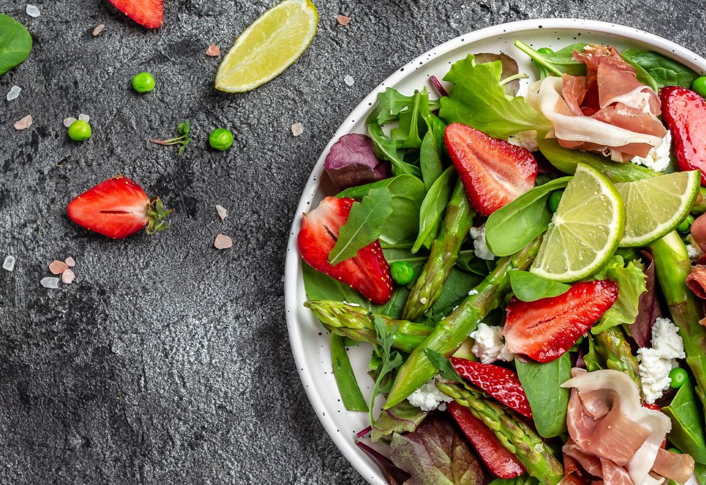 Schüssel mit gemischtem Salat aus Spinat, Erdbeeren, Limette und Nüssen auf dunklem Untergrund