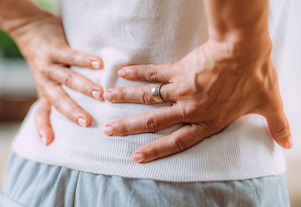 Person hält sich mit beiden Händen den unteren Rücken, Symbol für Rückenschmerzen