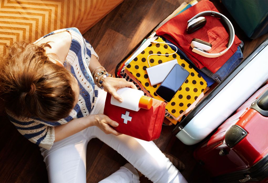 Frau sitzt neben geöffnetem Koffer und packt Kleidung und Urlaubsutensilien ein