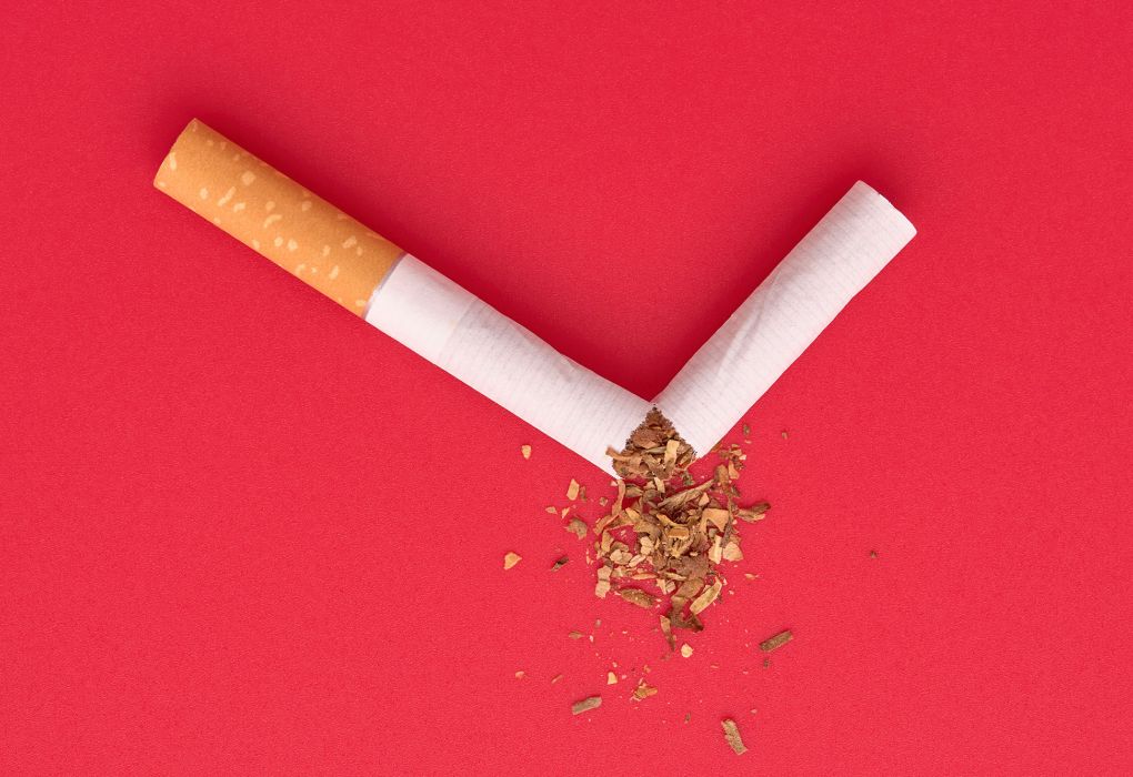 Zerbrochene Zigarette auf rotem Hintergrund, Symbol für Rauchstopp