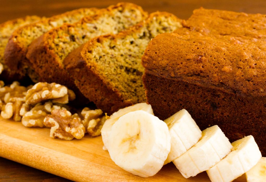 Geschnittenes Bananenbrot auf Holzbrett mit Walnüssen und Bananenscheiben dekoriert