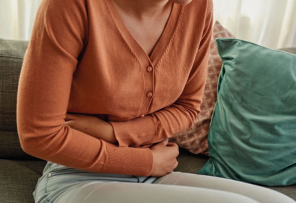 Frau hält sich den Bauch in einer Haltung, die Schmerzen ausdrückt.