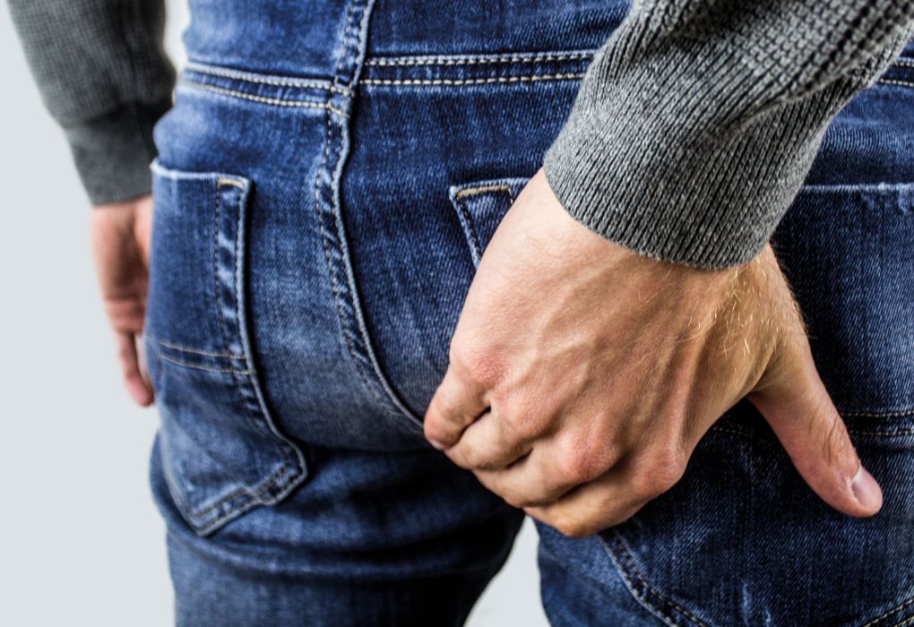 Mann in Jeans hält sich diskret das Gesäß als Hinweis auf Beschwerden.