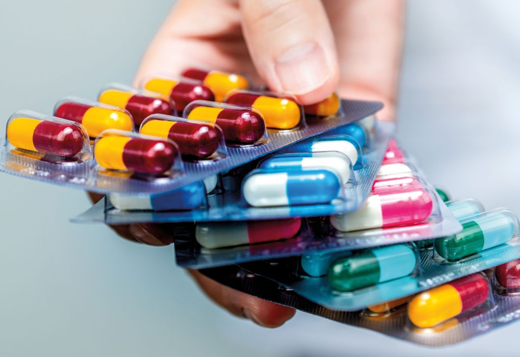 Hand hält mehrere Blisterpackungen mit bunten Kapseln und Tabletten