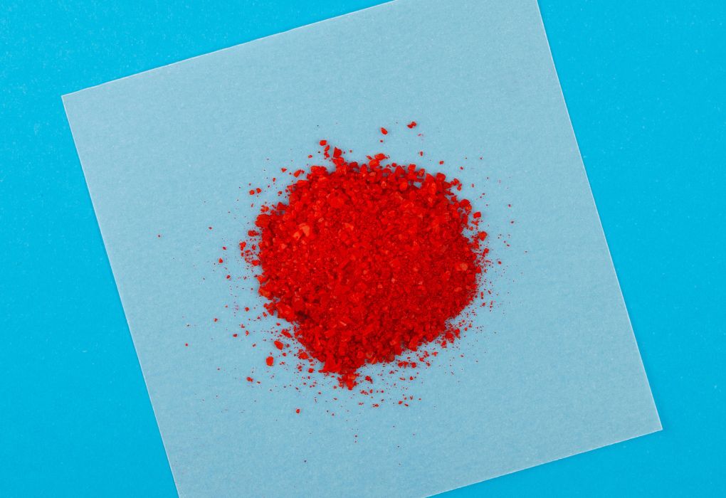 Heller Haufen roten Pulvers auf quadratischem weißen Papier vor blauem Hintergrund