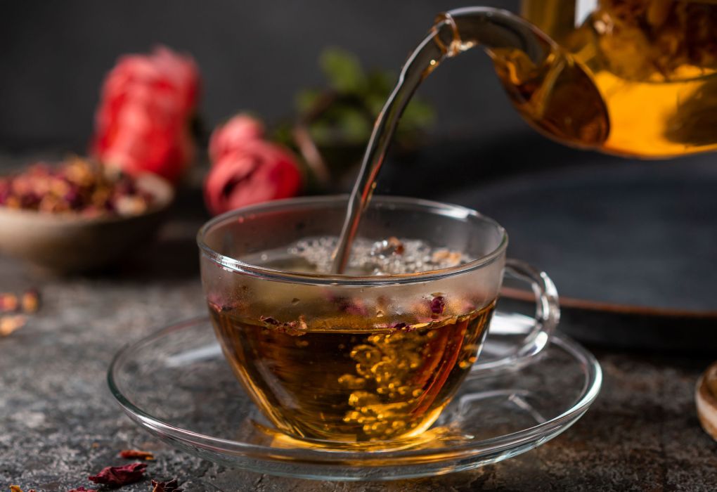 Frisch aufgegossener Tee wird aus einer Kanne in ein Glas eingeschenkt, dekoriert mit winterlichen Gewürzen