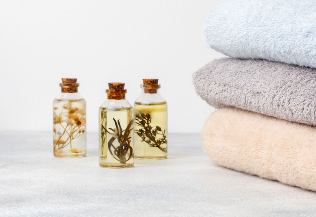 Kleine Fläschchen mit ätherischen Ölen neben gefalteten Handtüchern auf hellem Untergrund