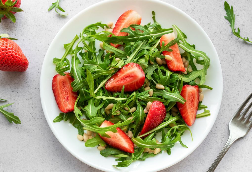 Teller mit grünem Rucolasalat und frischen Erdbeeren, angerichtet mit Dressing