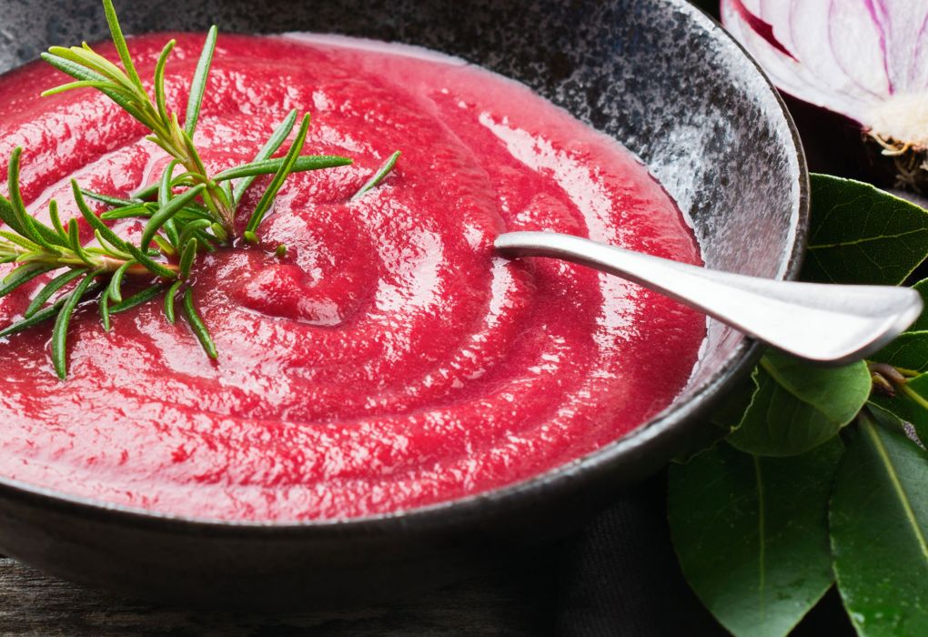 Teller mit roter Cremesuppe, dekoriert mit frischem Rosmarin und Löffel am Rand