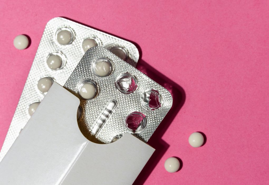 Blisterpackung mit Antibabypille auf pinkem Hintergrund, einzelne Tabletten liegen daneben