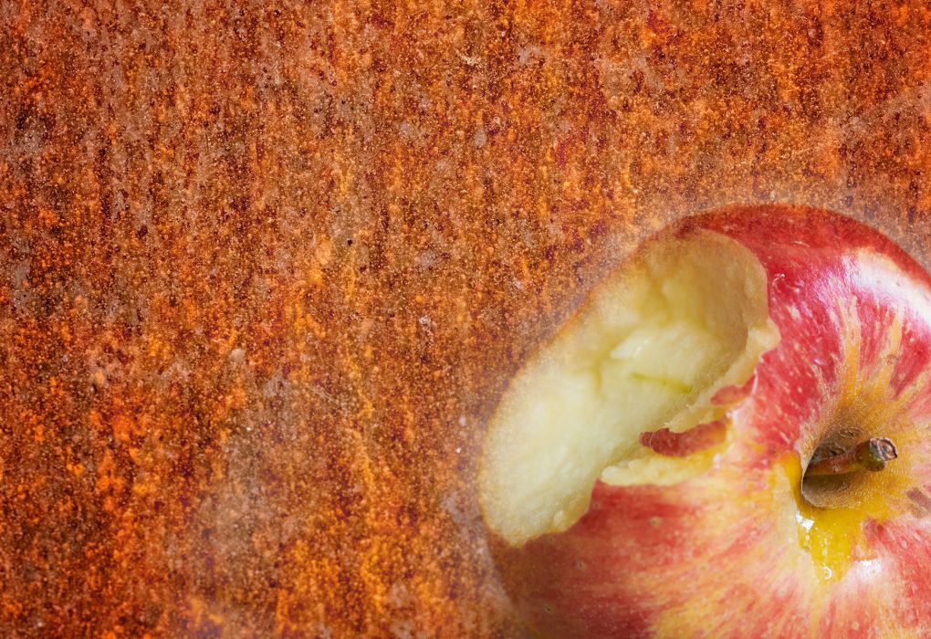 Rostige Metalloberfläche im Hintergrund, im Vordergrund ein angebissener Apfel