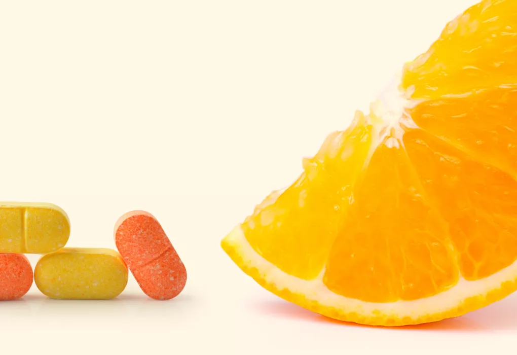 Aufgeschnittene Orange neben bunten Vitamin-Kapseln auf hellem Hintergrund