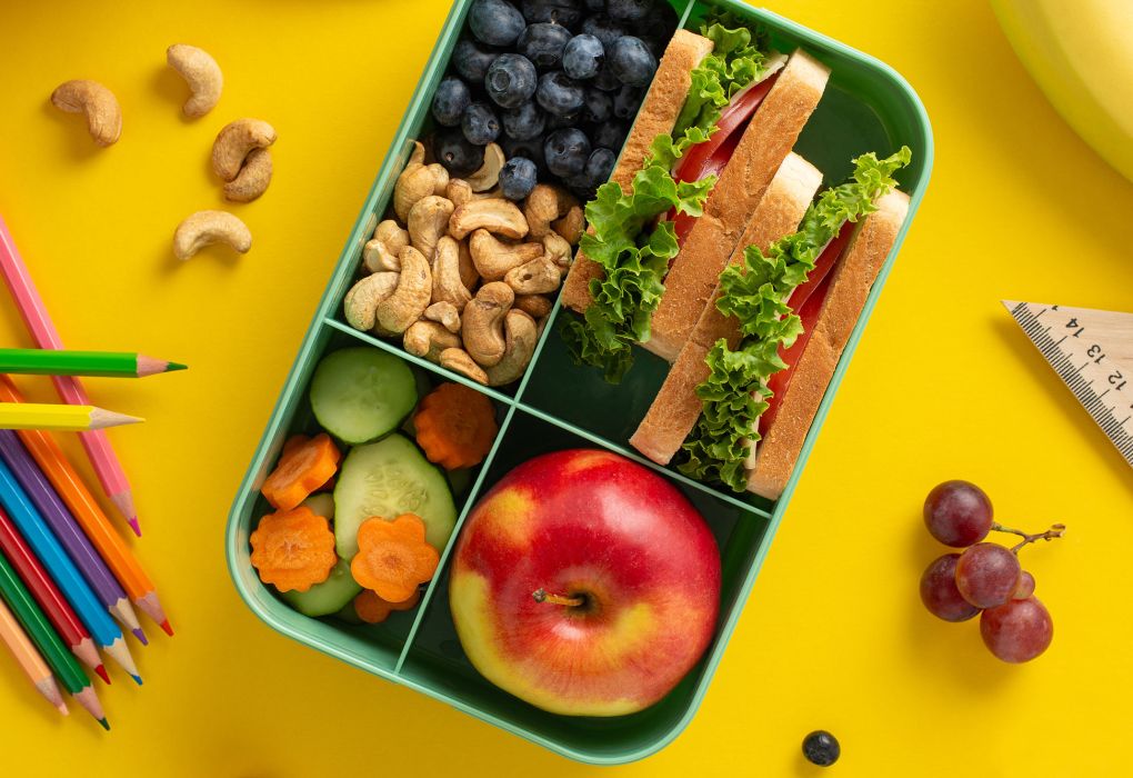 Bunte Brotdose mit Obst, Gemüse und Snacks auf gelbem Hintergrund