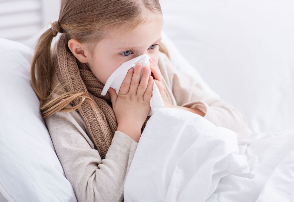 Mädchen sitzt mit Taschentuch im Gesicht und niest, Symbol für Erkältung oder Schnupfen